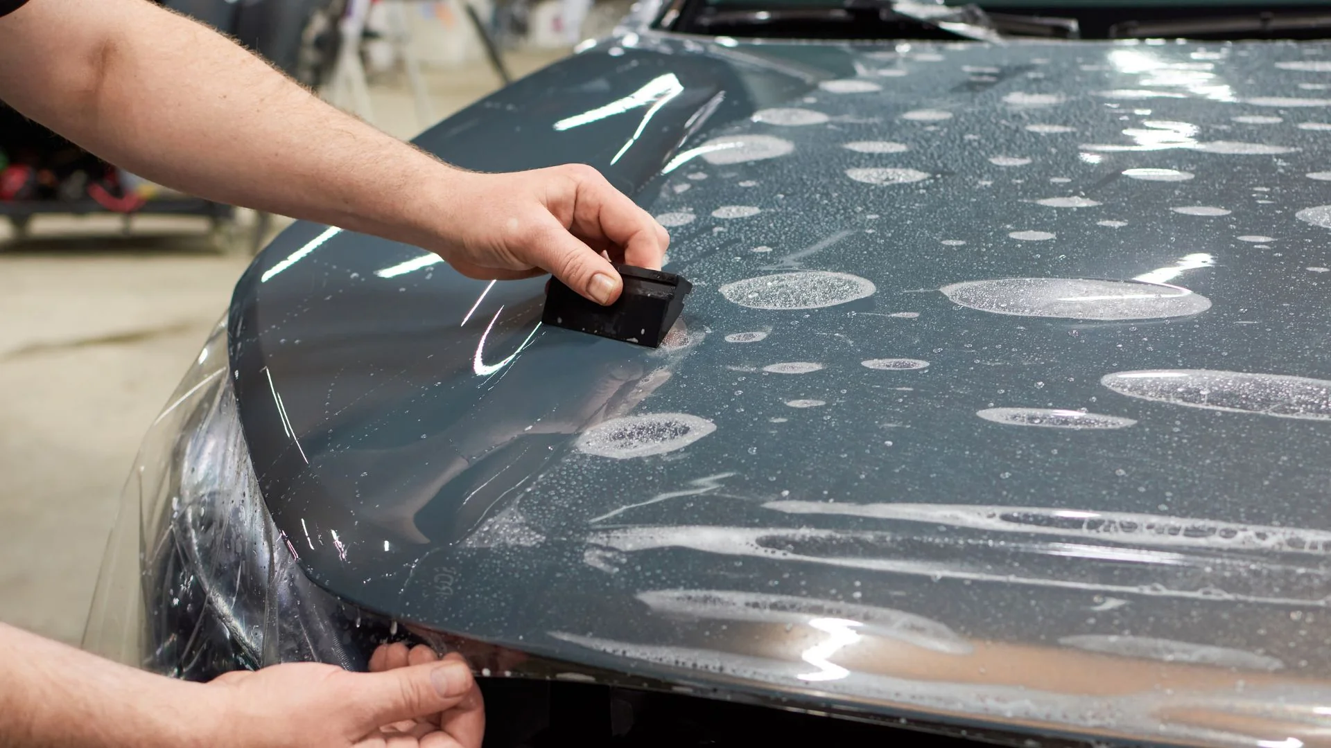 Paint protection film being installed on a vehicle hood with squeegee and water